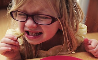 A little girl with glasses who is a picky eater, eating a vegetable in disgust