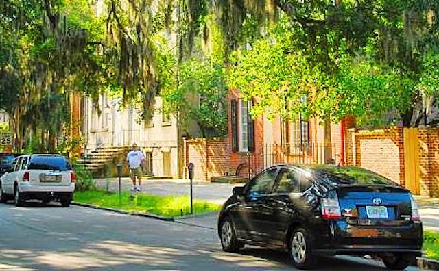 A neighborhood with big pretty houses and two cars parked on the street