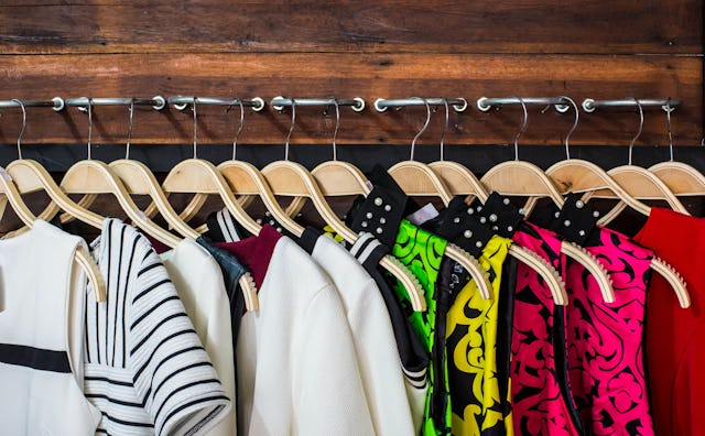 A row of multiple colored dresses on wooden hangers, hanging on metal poles attached to the wood