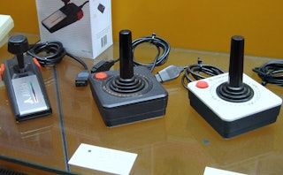 Three older joysticks lined up on a table 