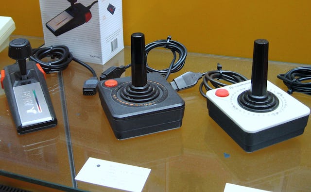 Three older joysticks lined up on a table 