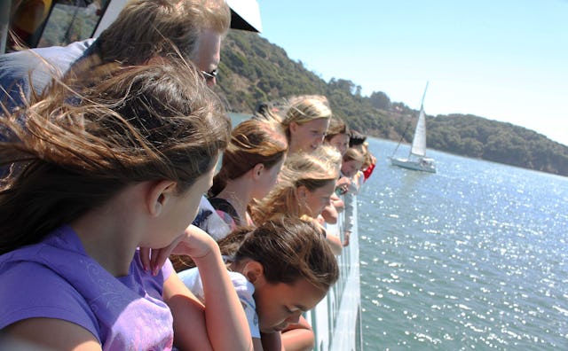 A parent chaperoning a group of middle-schoolers enjoying a sunny boat ride during the field trip.