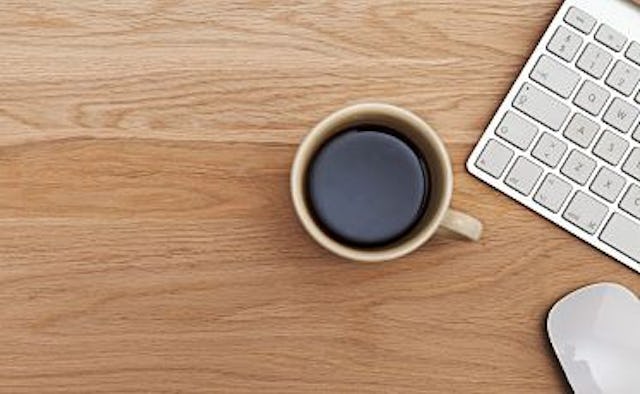 A cup of coffee, a laptop and a mouse on a wooden desk 