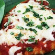 Piece of chicken parmigiana garnished with greens on top