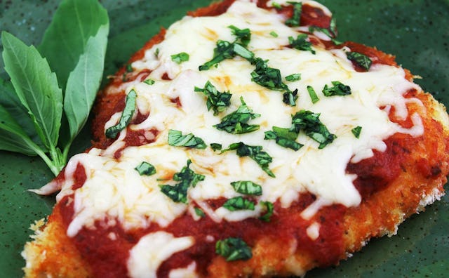 A piece of chicken parmigiana garnished with greens on top