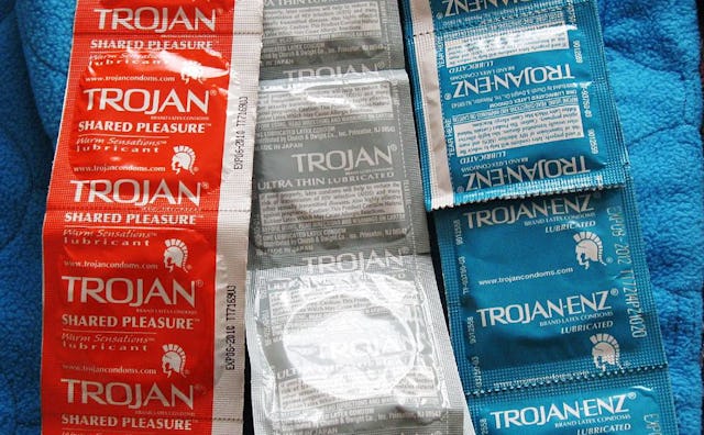 Three multi-packs of red, grey, and blue Trojan condoms on a blue blanket