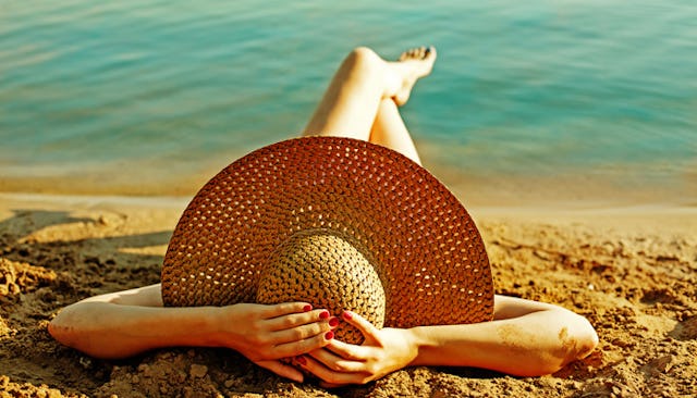 A woman with a large straw hat sunbathing on a beach enjoying her pre Mother's Day