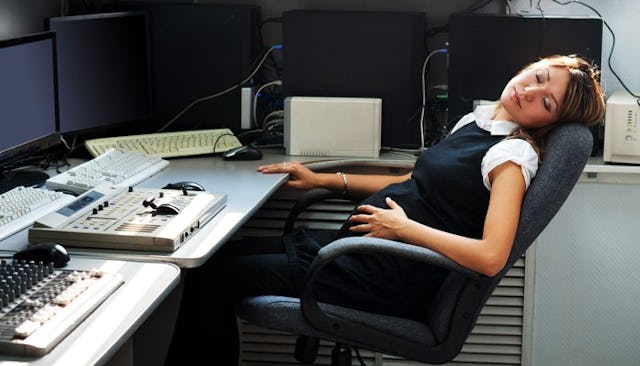 A pregnant woman in the office lying down on a chair in front of her desk