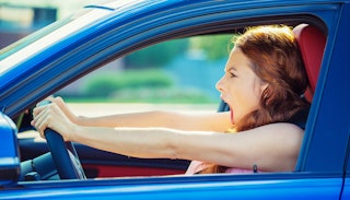 A woman holding on to the steering wheel of her car and screaming