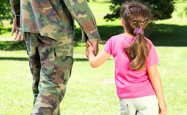A military kid walking and holding her father's hand and the father is wearing a camo print uniform
