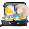 An opened black suitcase packed with a beach ball, summer hat, towels, and flip-flops