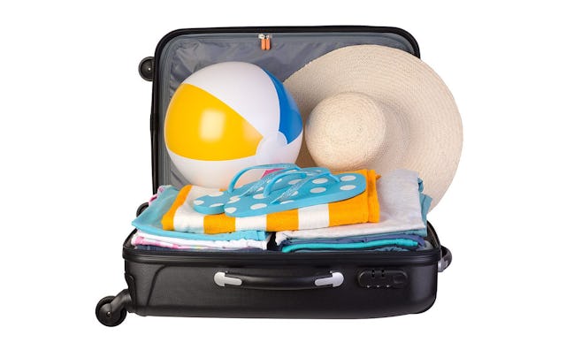 An opened black suitcase packed with a beach ball, summer hat, towels, and flip-flops