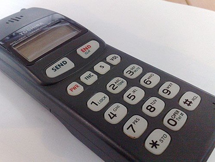 An old black Toshiba cellphone with white buttons on a white surface