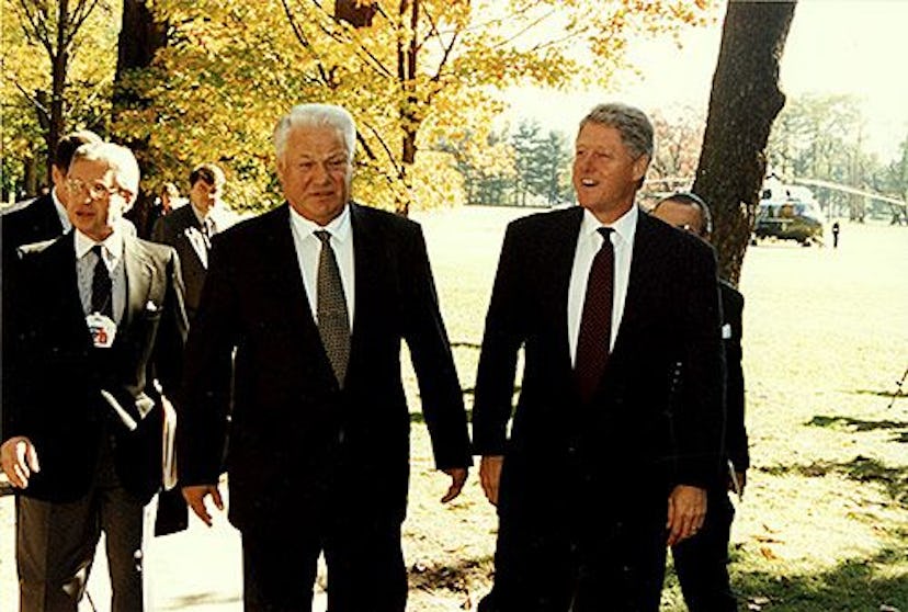 Boris Yeltsin and Bill Clinton walking through a park with a group of men walking behind them