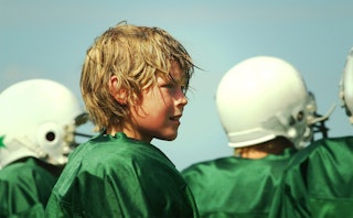 A blonde boy with long hair playing rugby with his teammates.