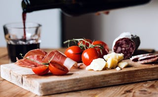 Bacon, cherry tomatoes, and cheese on a cheeseboard on top of a kitchen counter