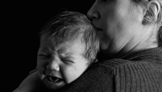 A baby crying on his mothers shoulder while she comforts him