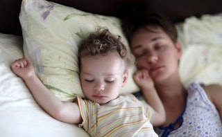 A mom co-sleeping with her baby on white sheets and yellow pillows