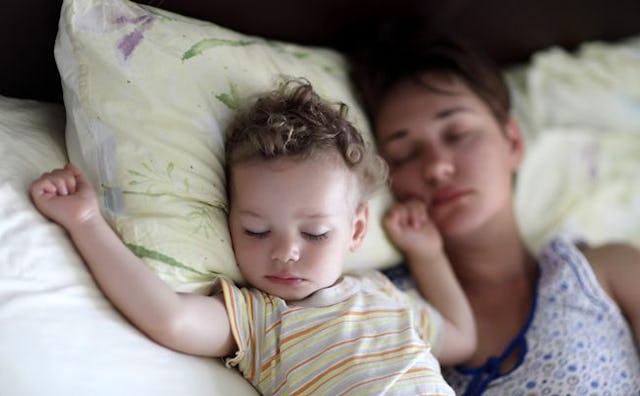 A mom co-sleeping with her baby on white sheets and yellow pillows