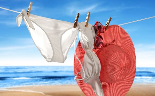 A white bikini a mom can wear and a red hat hanging on a drying rope on a beach during a sunny day