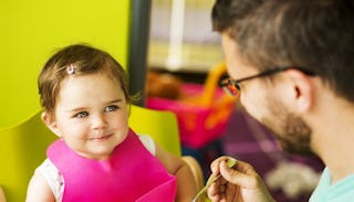 A gay dad feeding his baby with a yellow wall in the background