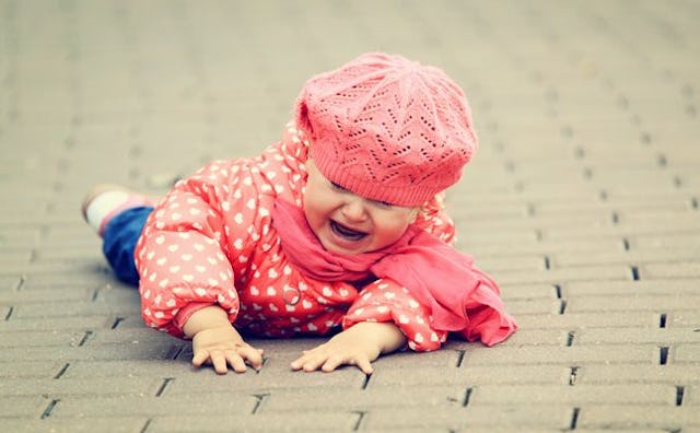 A 2-year-old girl in a pink puffer jacket and pink beanie on the ground crying
