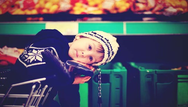 A toddler boy with a beanie sitting on a shopping cart