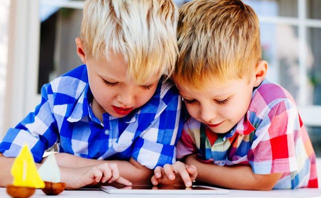 Two blonde boys in a blue and in a red checked shirt looking at a phone