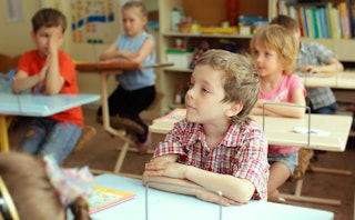 Elementary school kids sitting next to their desks during class