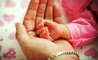 A close-up of a woman's hand with a bracelet and a newborn's hand on it