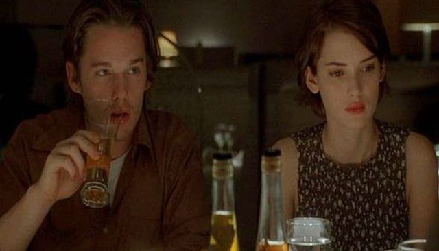 Ethan Hawke in a burgundy shirt drinking a coke and Wynona Rider in a sleeveless top sitting at a t...