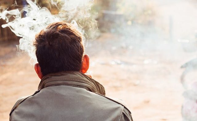A middle-aged from the back in a grey jacket man chain smoking and thinking about how to stop smokin...