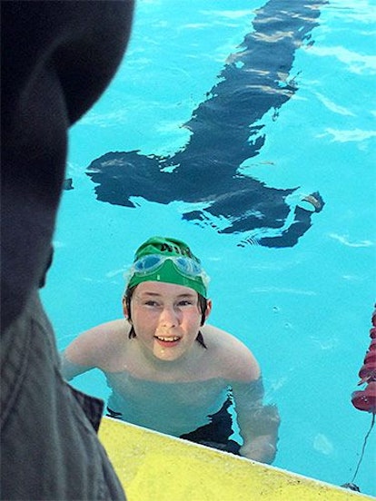 A boy, fresh out of the pool, sporting a swim cap and goggles, during his first swim meet