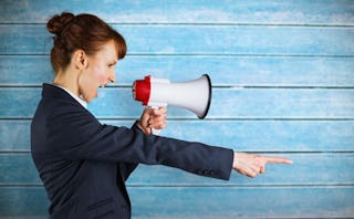 A woman in a suit yelling with a megaphone with a blue wall behind her