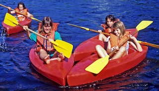 Four children in red canoes on the clear blue water paddling and laughing