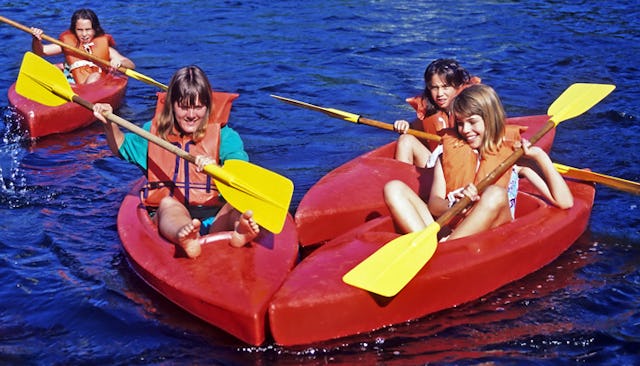 Four children in red canoes on the clear blue water paddling and laughing