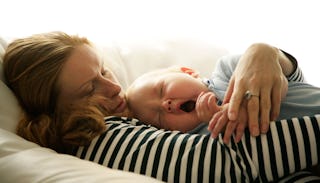 A mother holding a baby on her chest while the baby is jawning