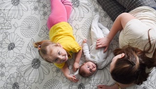 A woman lying on the floor with her baby and toddler daughter