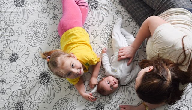 A woman lying on the floor with her baby and toddler daughter