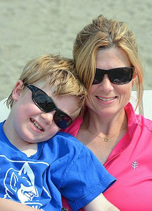 A woman in a pink polo shirt and black sunglasses holding her brown-haired son in a blue T-shirt and...