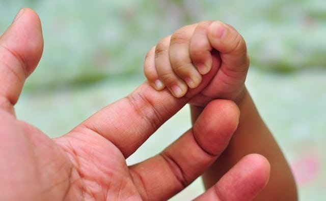 A close-up of a baby's hand holding his dad's finger