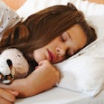 A young brunette girl sleeping with her stuffed toy tiger and teddy bear