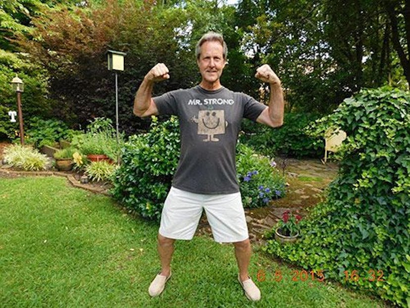 A father standing in a garden flexing his muscles, dressed in white shorts and a black t-shirt.