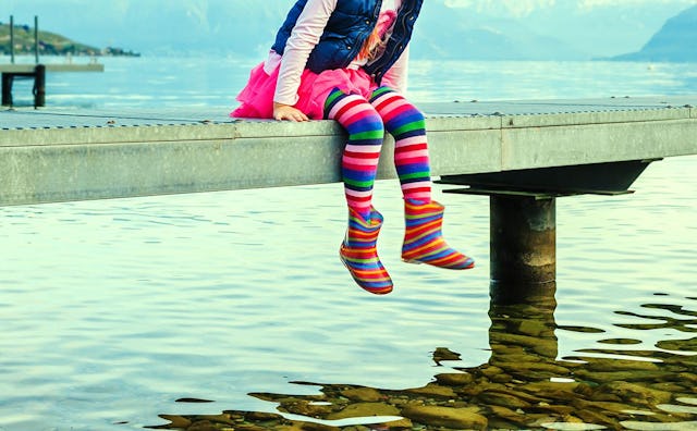 Little girl with colorful leggings and boots sitting on the small dock