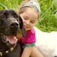 A little girl with a tiara and a tutu hugging her dog while sitting outside