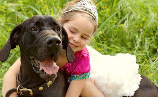 A little girl with a tiara and a tutu hugging her dog while sitting outside