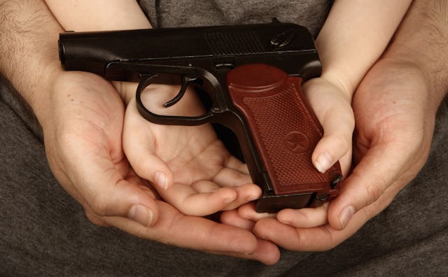 A close-up of a father's hands holding a child's hand that's holding a gun