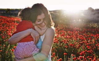 A mother holding her daughter in a poppy field on a sunny day