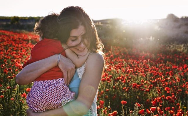 A mother holding her daughter in a poppy field on a sunny day