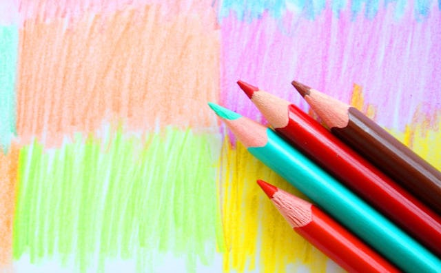 Four differently-colored coloring pencils on top of a colored paper for arts and crafts activities